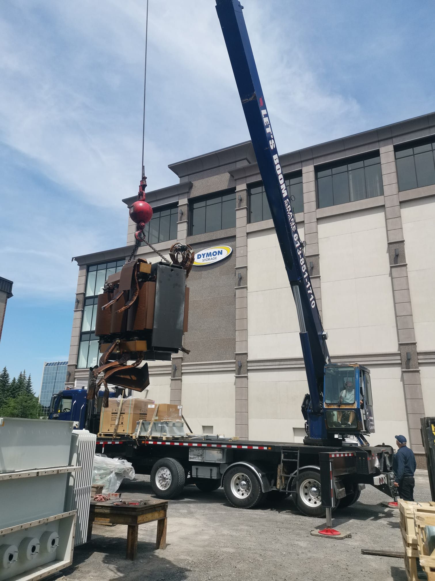 A crane is lifting a large object from a truck in front of a building.