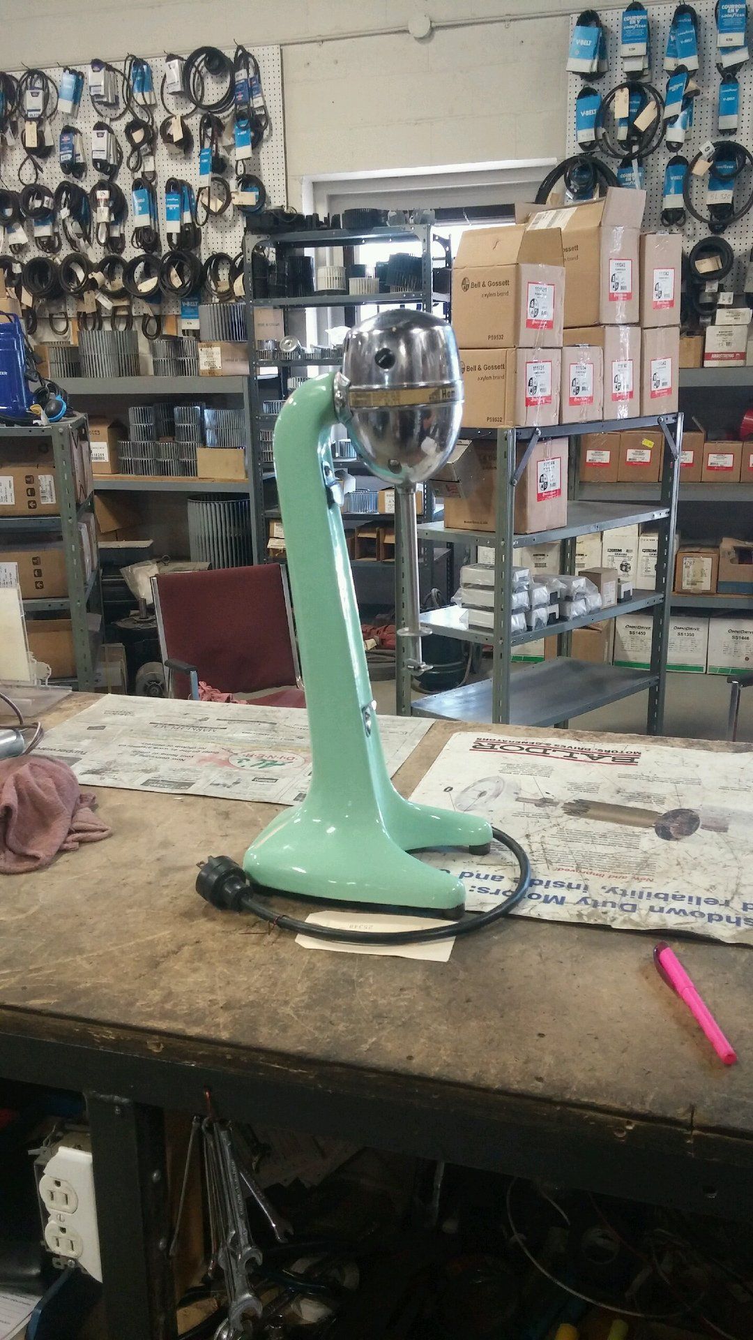 A green fan is sitting on top of a wooden table in a warehouse.