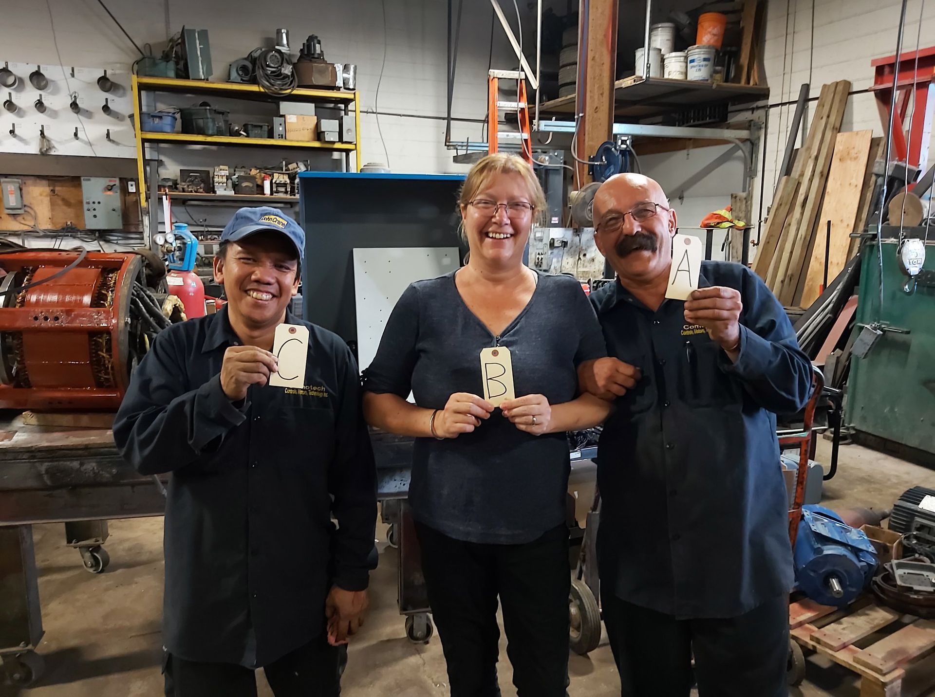 Three people are standing next to each other in a garage holding cards.