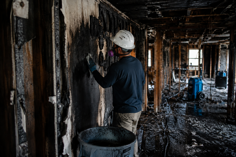 Restoration professional removing soot from fire-damaged wall