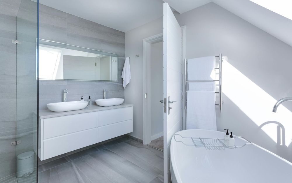 A modern bathroom featuring a white vanity with two vessel sinks, a glass-enclosed shower, and a freestanding bathtub.