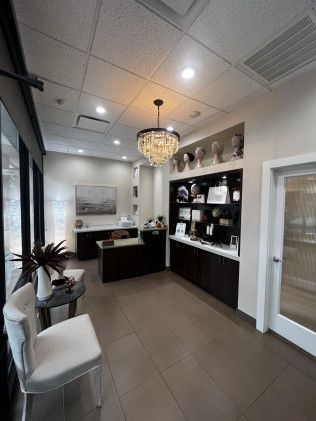 Reception area with desk, seating, and decorative shelving; a chandelier hangs from the ceiling.