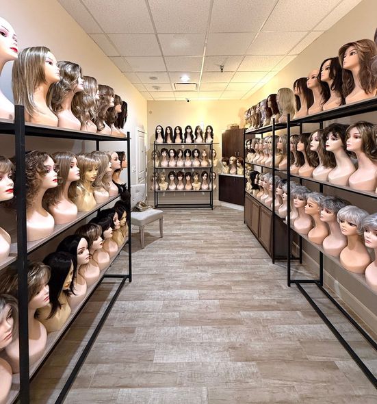 Wig store interior, many wig-covered mannequins line shelves. Blond, brown, and gray wigs displayed on racks.