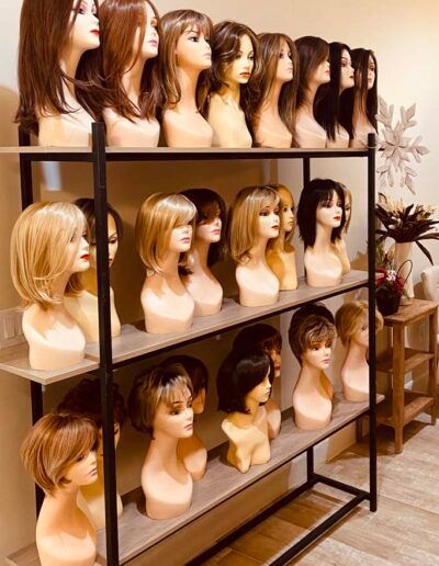 Wigs displayed on mannequin heads arranged on shelves in a shop. Various styles and colors are visible.