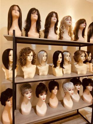 Wigs displayed on mannequin heads, arranged on shelves. Various styles and colors are visible.