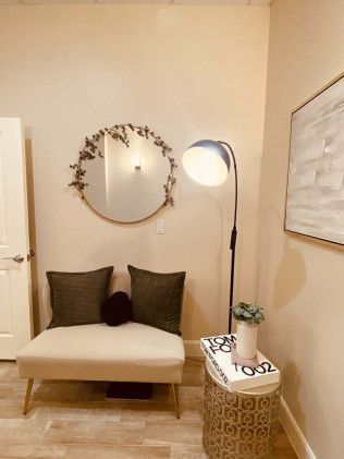Beige seating area with a mirror, floor lamp, and side table against a neutral wall.