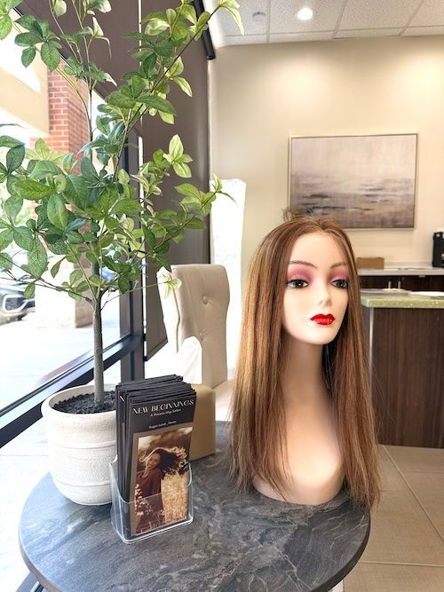Mannequin with long, light brown hair. Displayed on a table in a store setting, near a potted plant.