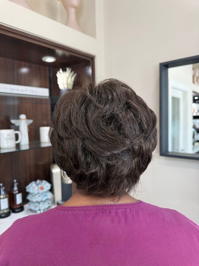 Back view of a person with short, dark, textured hair; wearing a purple shirt, in a salon.