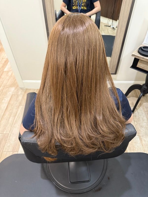 Person with long, light brown hair sits in a salon chair, back to the camera.