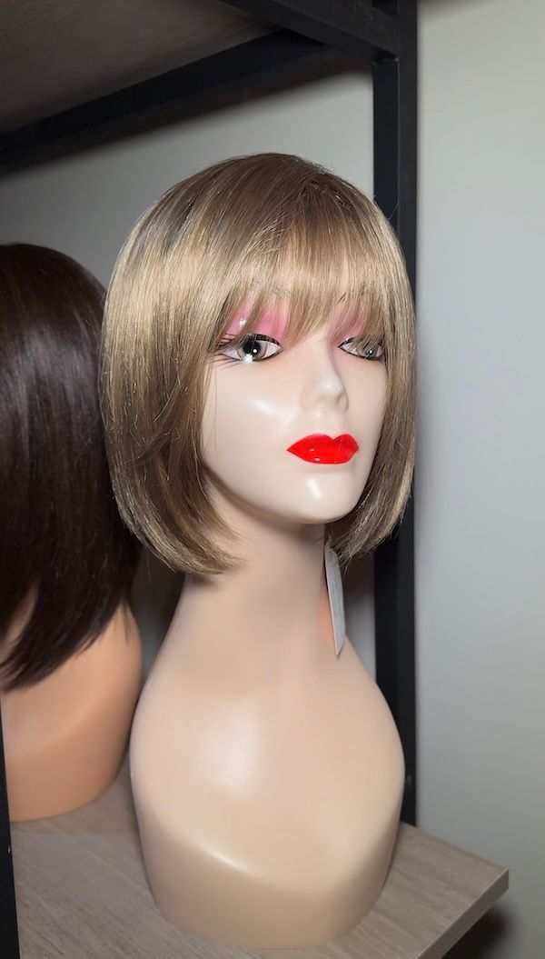 Mannequin head wearing a short, blonde wig with bangs and red lipstick.