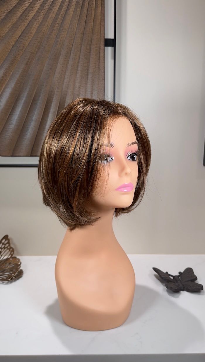 Mannequin head with brown bob wig, on white surface, against wall with art.