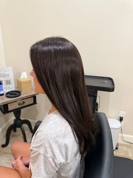 Woman with straight, dark brown hair, sitting in a chair. In a salon setting.