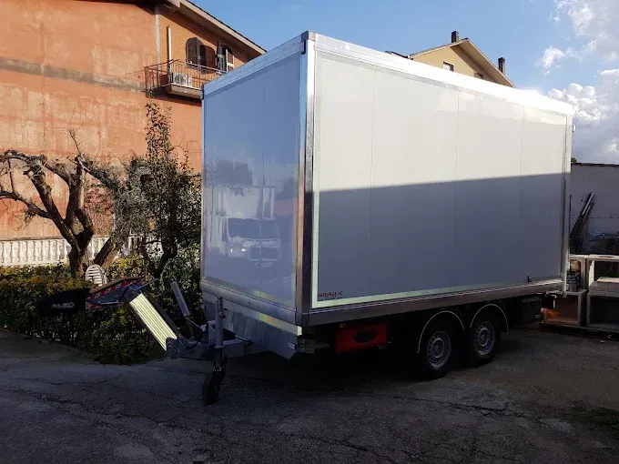 Un furgone bianco parcheggiato in strada accanto a un edificio e a un albero spoglio.