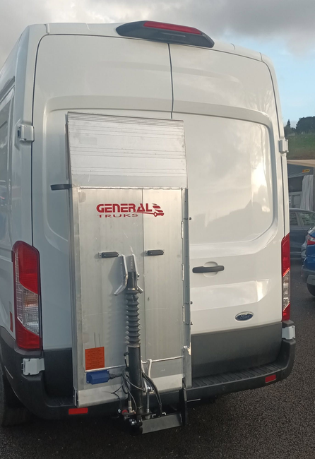 Furgone bianco con sollevatore per sedie a rotelle montato posteriormente, parcheggiato all'aperto.