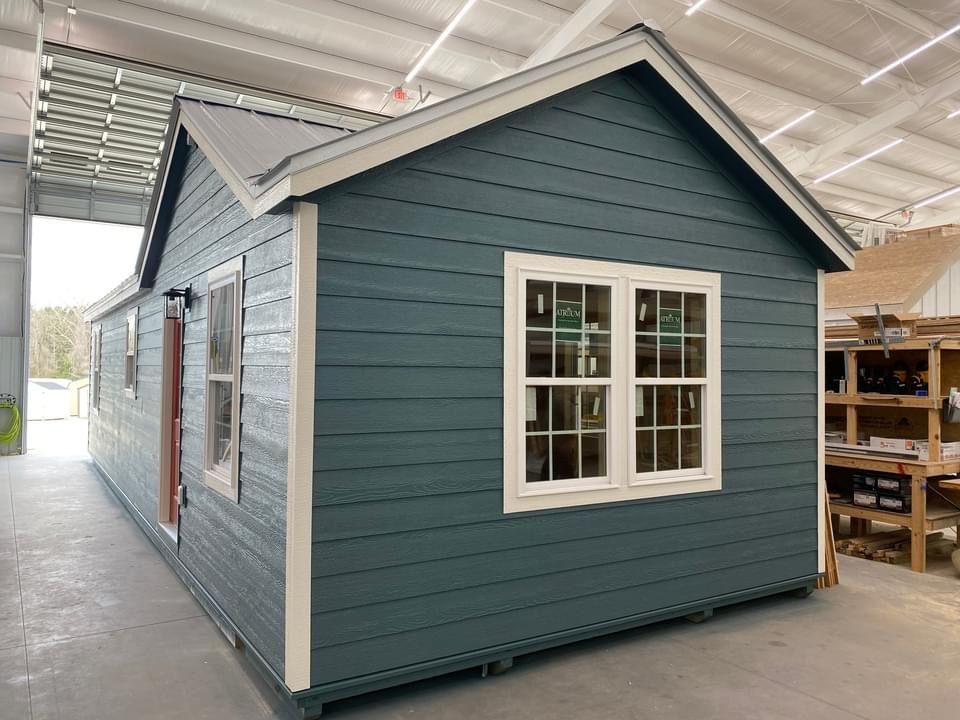 A small blue house with white windows is being built in a factory.