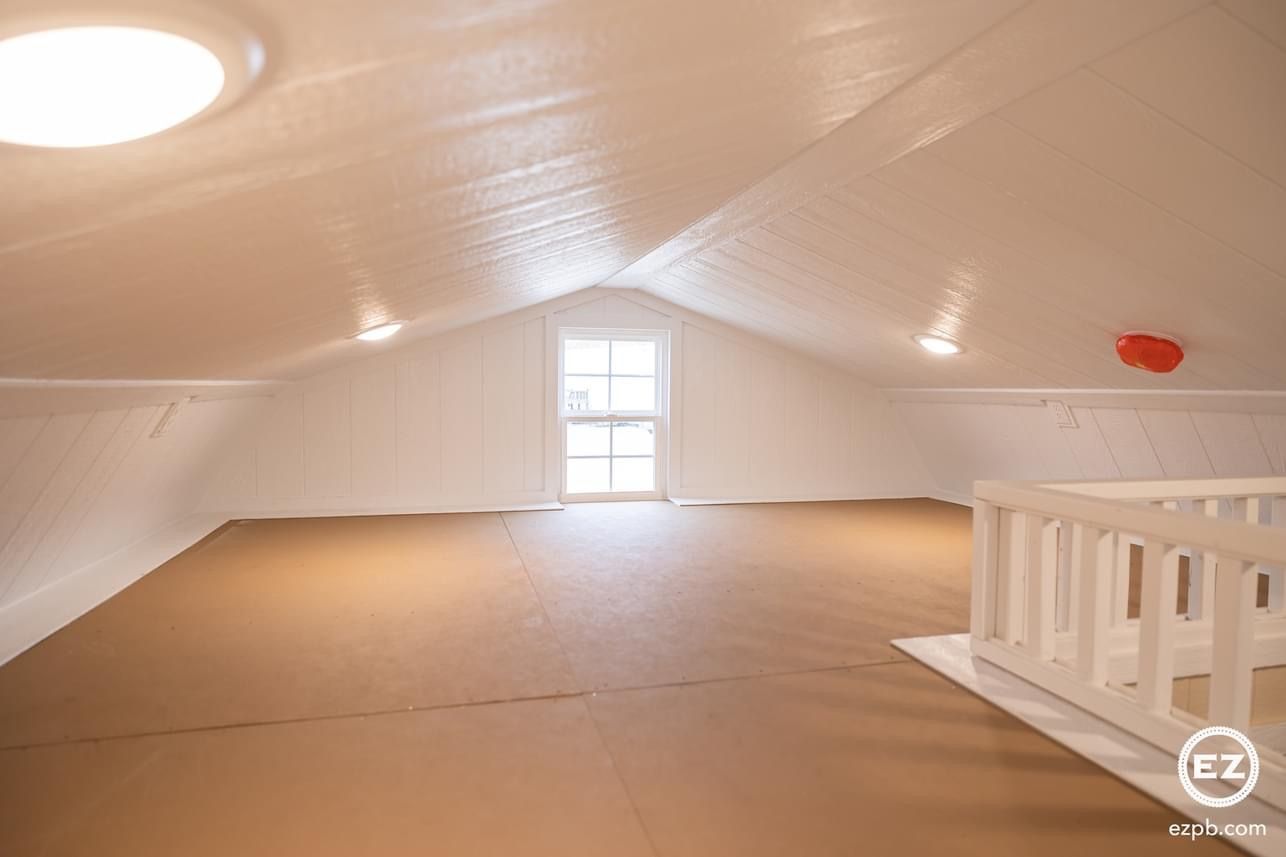 An empty attic with a staircase and a window.