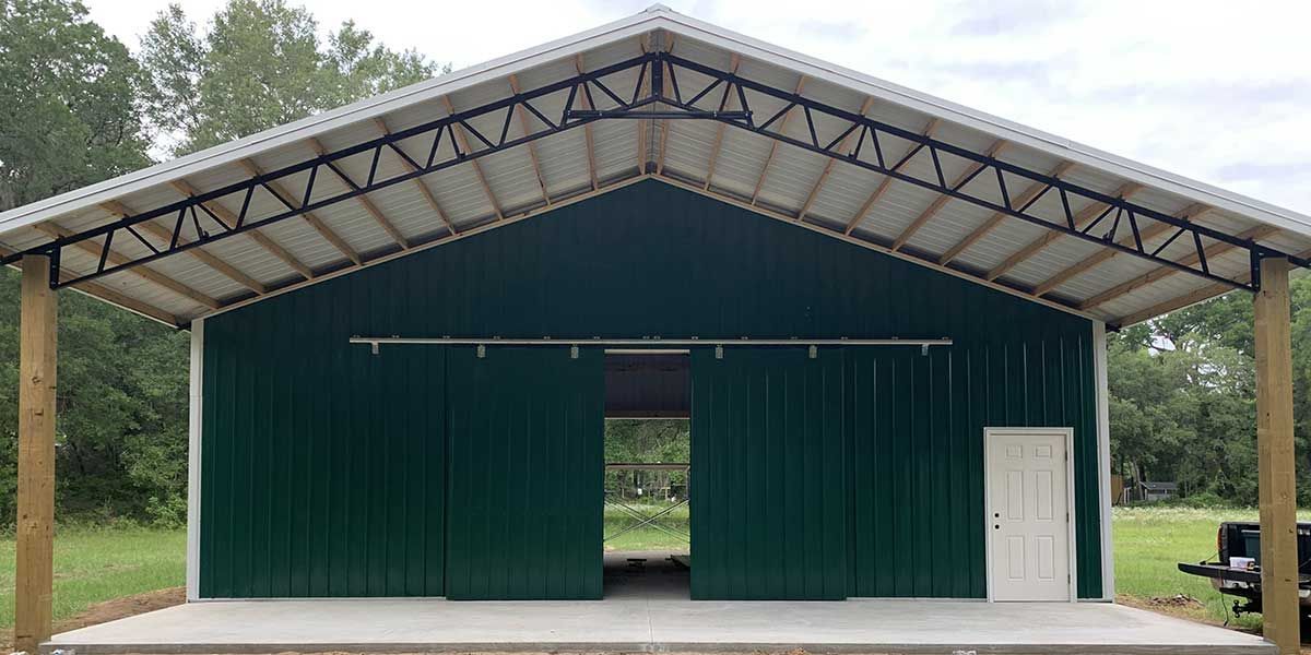 A large green barn with a white roof and sliding doors.