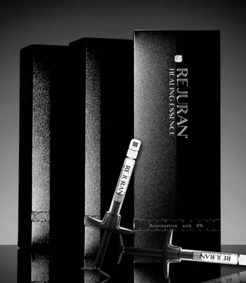 Black cosmetic packaging with two silver lip gloss tubes on a dark background