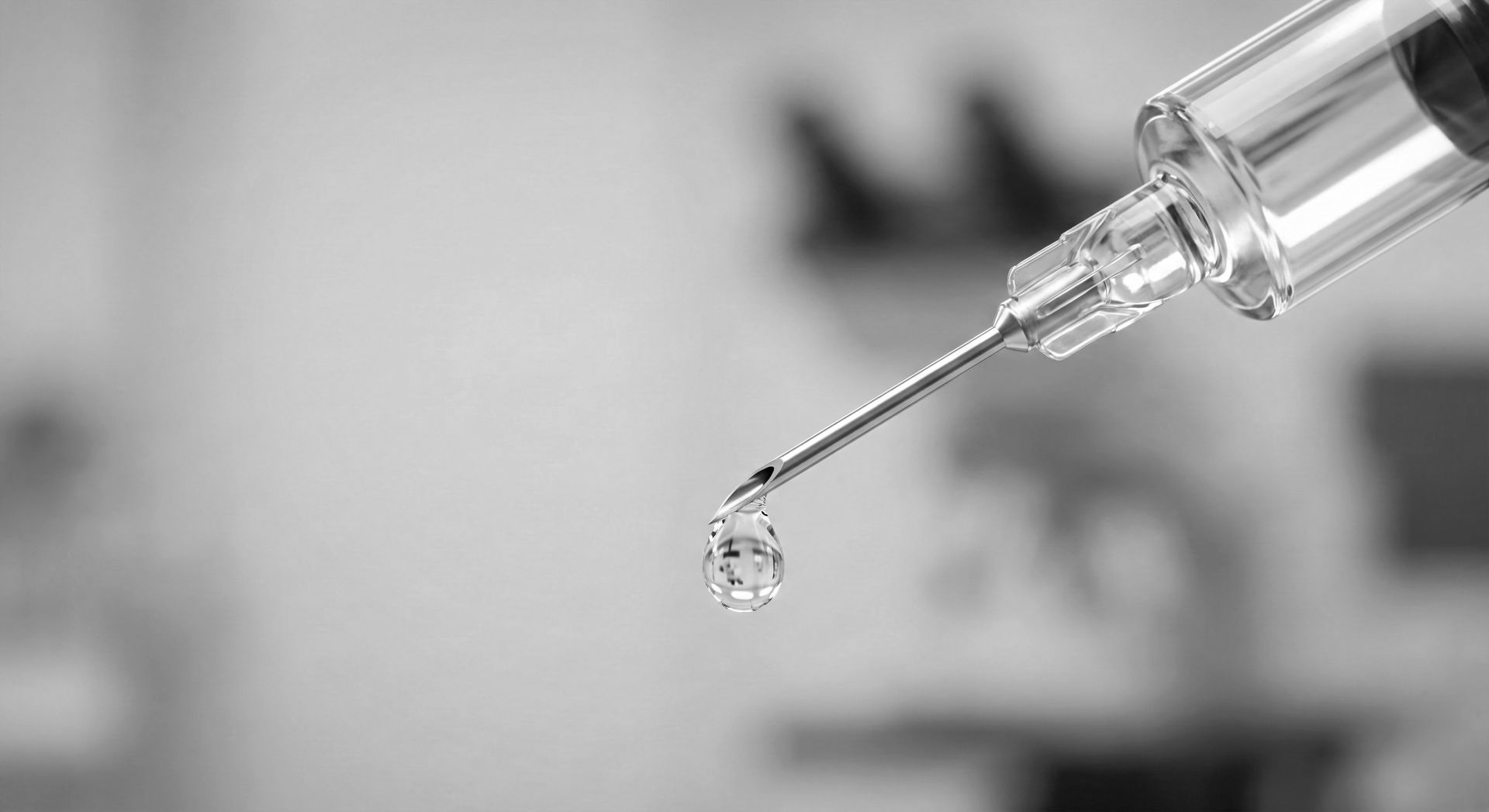 Close-up of a syringe with a droplet at the needle tip against a blurred background
