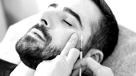 Gloved hands injecting a man’s cheek with a syringe during a facial treatment