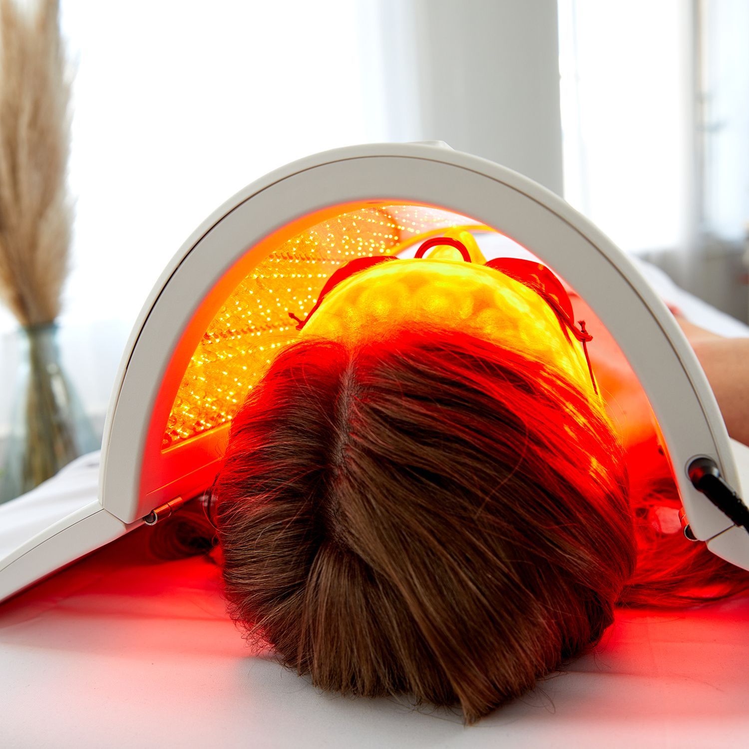 Person lying face down under a glowing red light therapy hood in a room