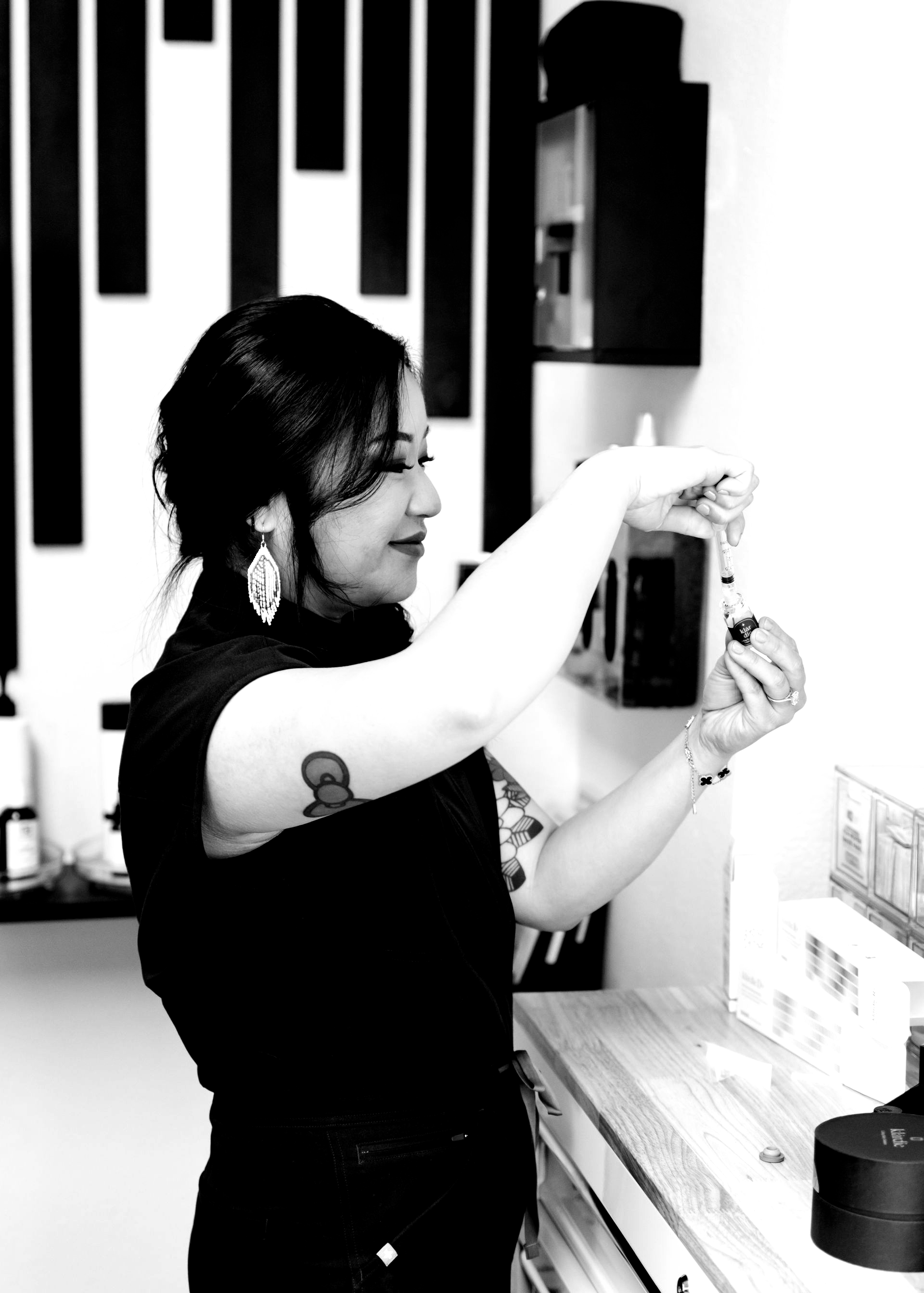 Woman applying makeup in front of a mirror, holding a small container in a black-and-white room.