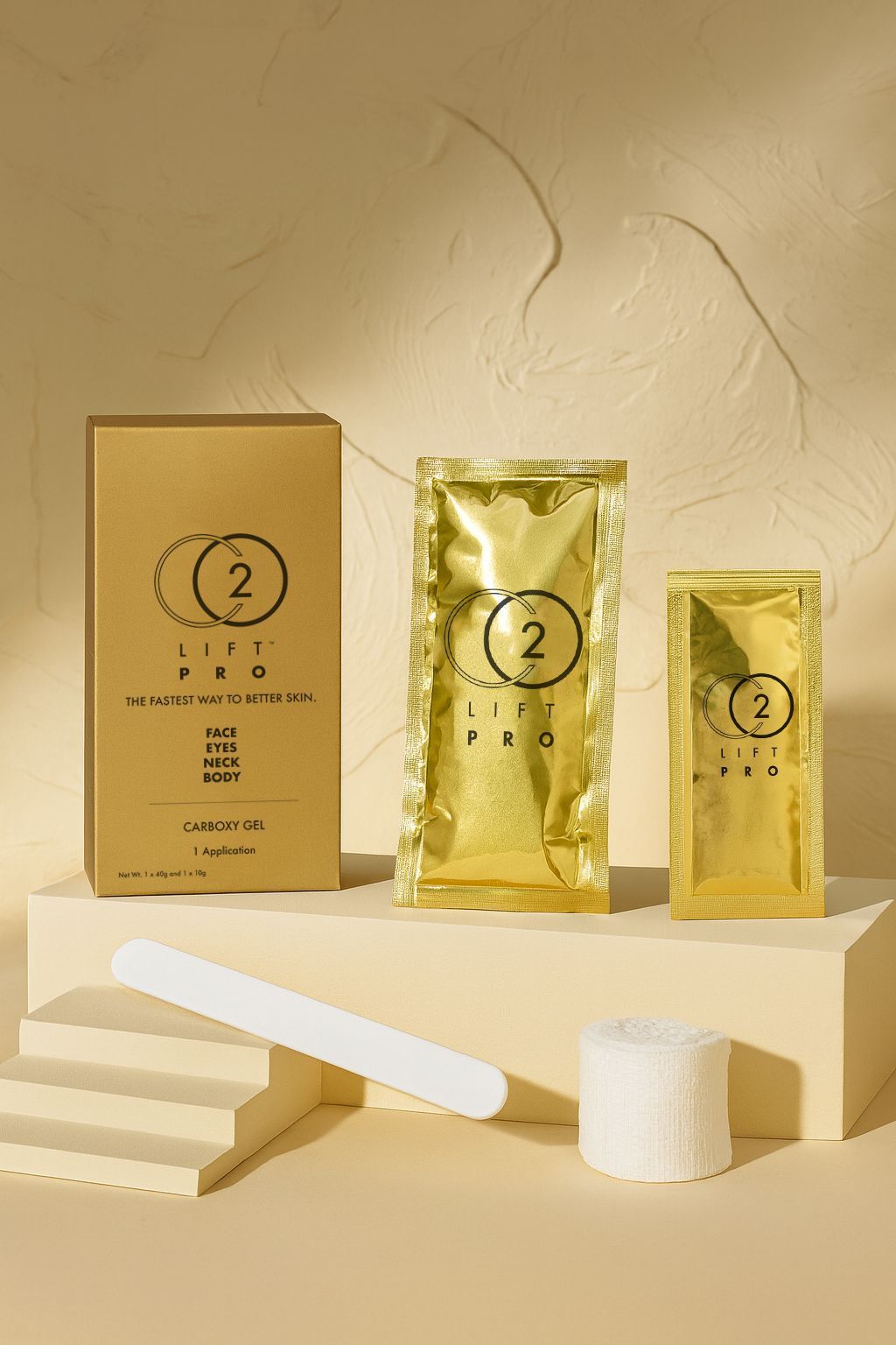 Gold skincare product packaging and sachets on a beige display with folded white paper accents