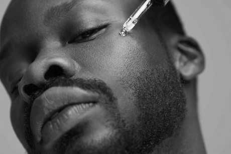 Close-up black-and-white portrait of a man with a dropper near his eye, looking calm