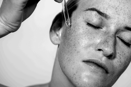 Close-up of a face with eyes closed as liquid is dripped onto the forehead from a dropper
