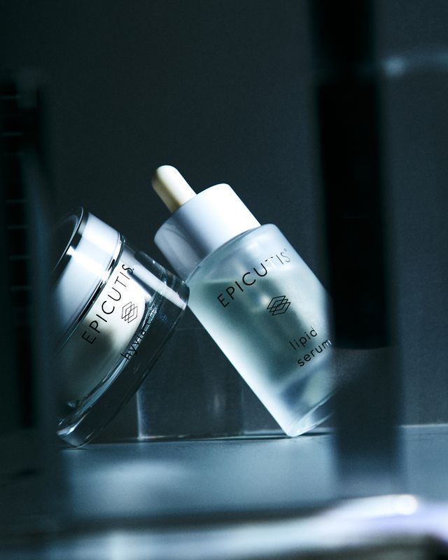 Two EPICUT silver skincare bottles on a dark reflective surface, one tilted against the other.