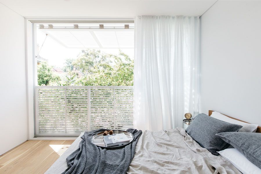 Bright bedroom with an unmade bed, white curtains, and a large window overlooking greenery. — Fineworx Joinery in Newcastle, NSW