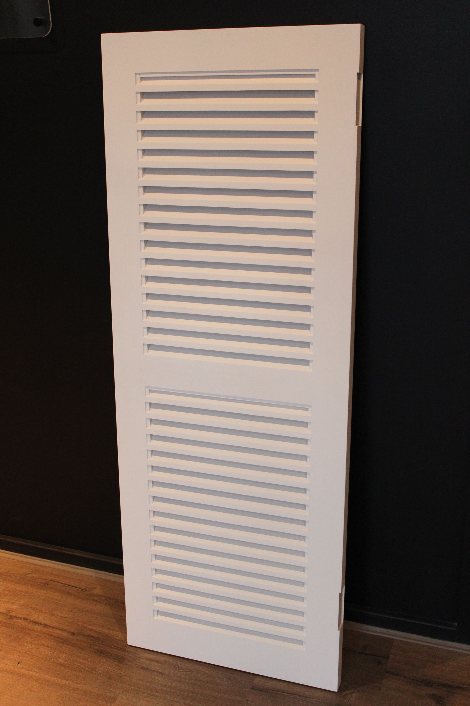 White louvered vent panel leaning against a dark wall on a wooden floor. — Fineworx Joinery in Warnervale, NSW