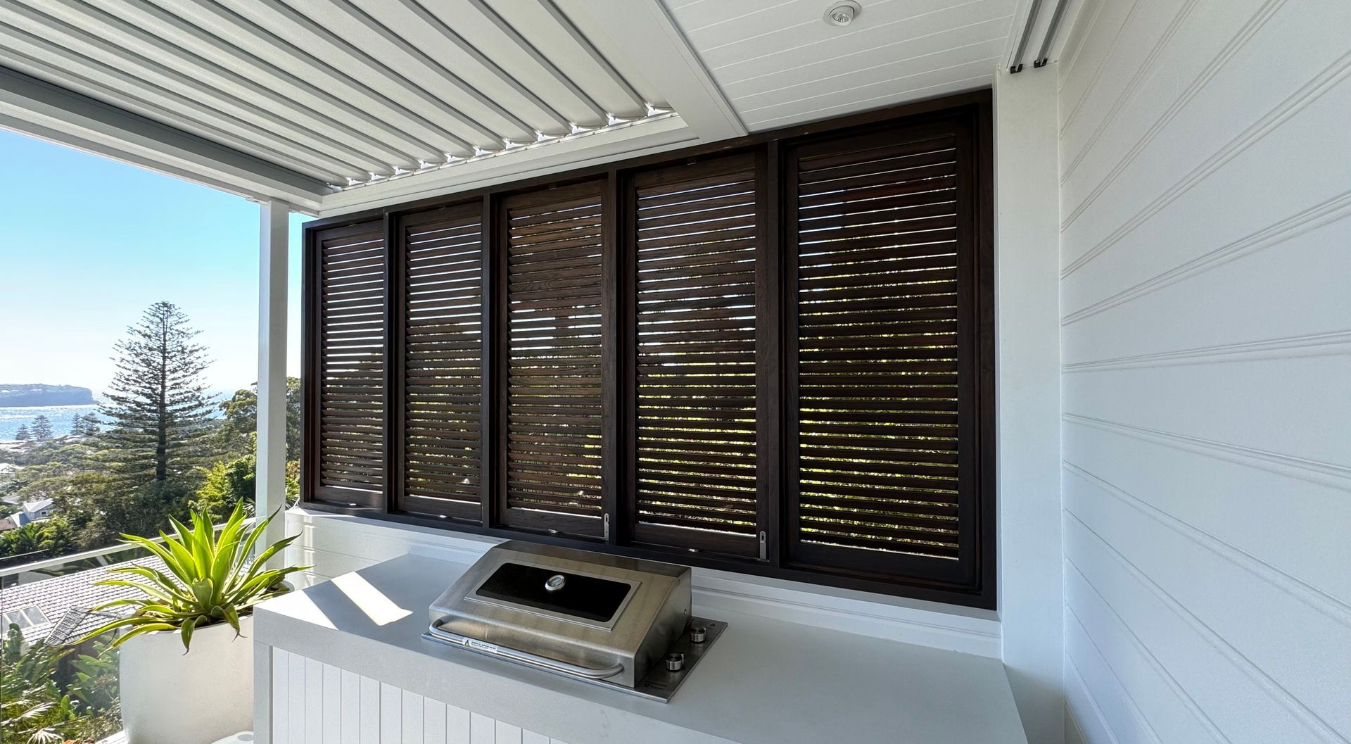 Covered Patio With Dark Louvered Shutters, Barbecue Grill, and Ocean — Fineworx Joinery in Warnervale, NSW