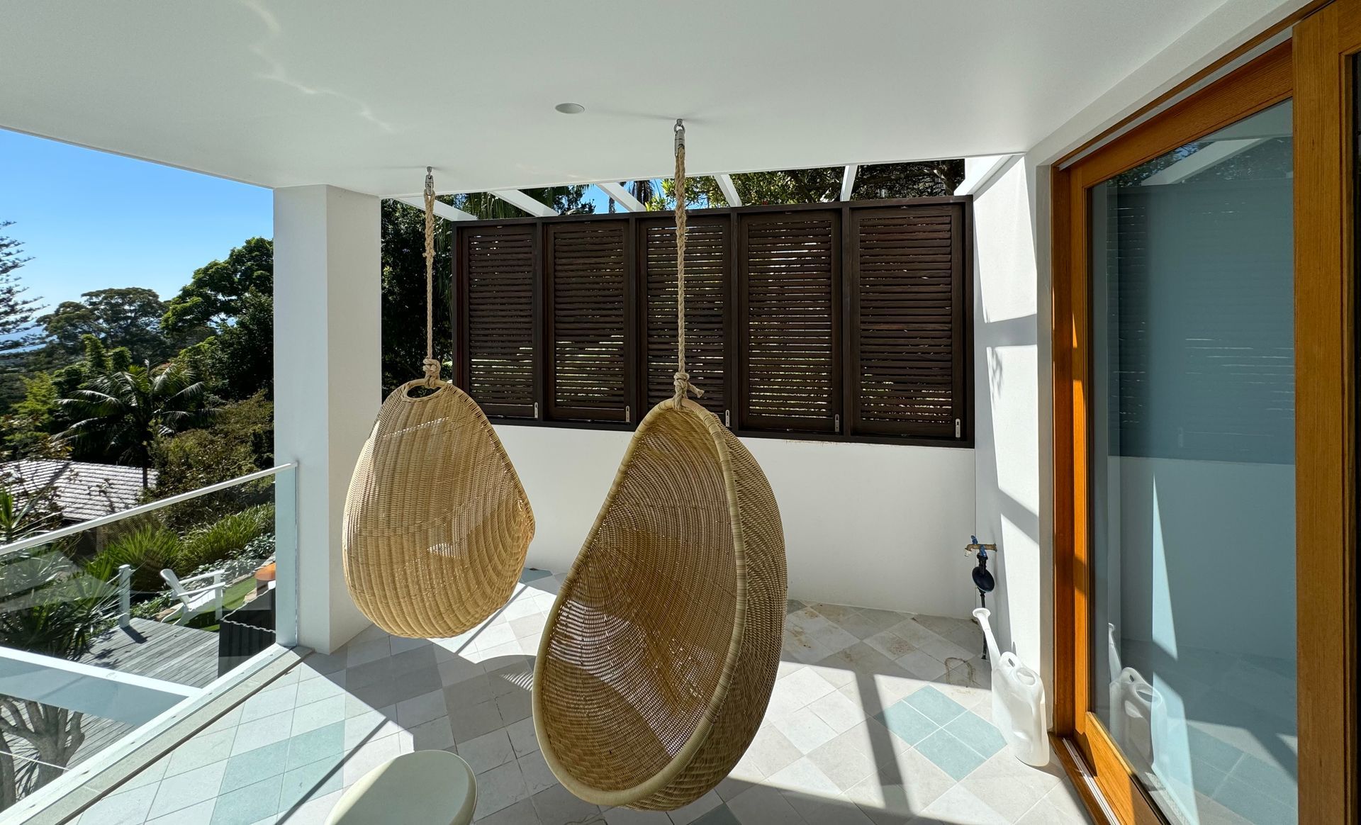 Two Woven Egg Chairs on a Sunny Balcony With Glass Railing and Wooden Shutters — Fineworx Joinery in Warnervale, NSW