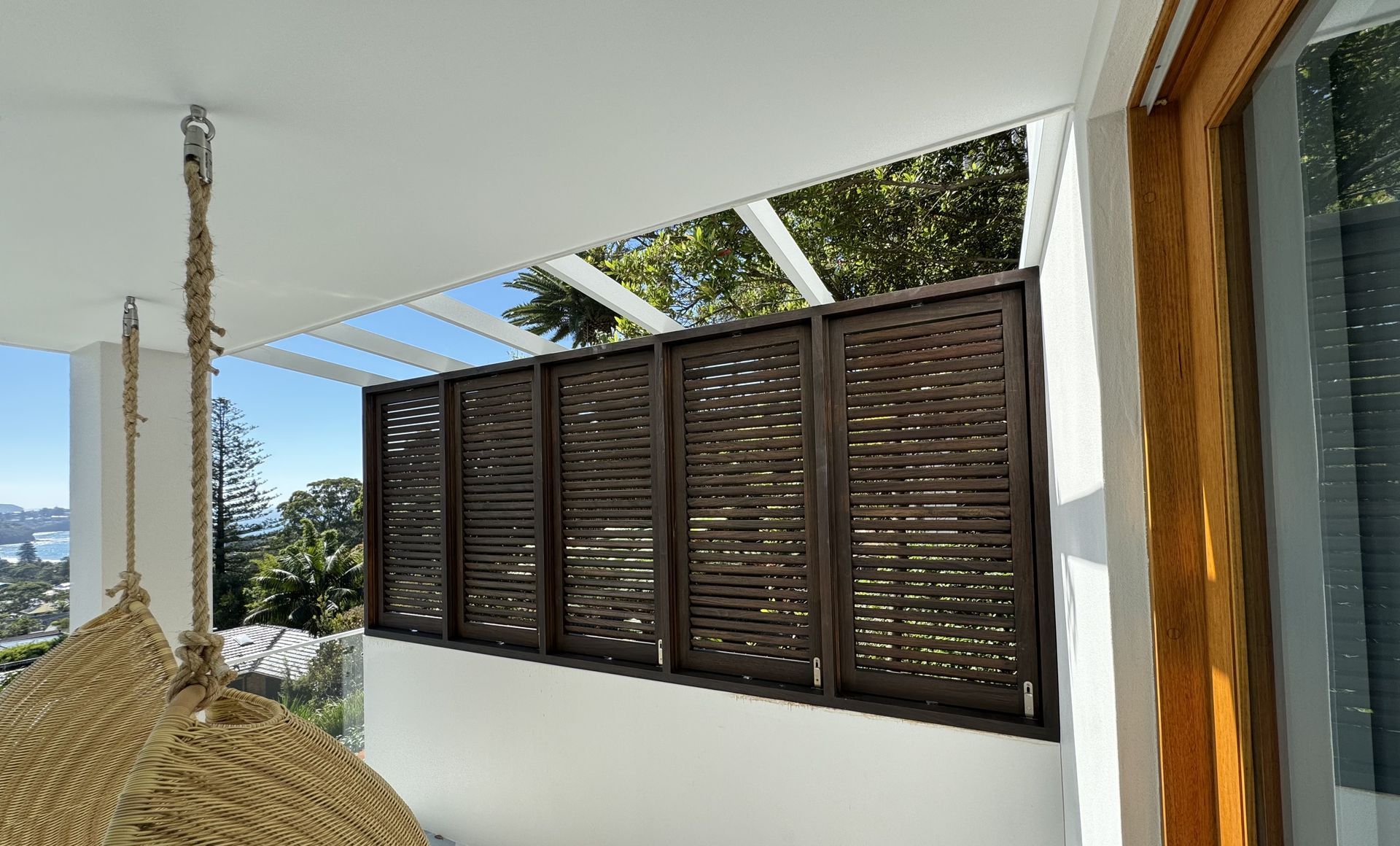 Balcony With Dark Wooden Shutters, White Walls, and a Hanging Woven Chair Overlooking Greenery — Fineworx Joinery in Warnervale, NSW