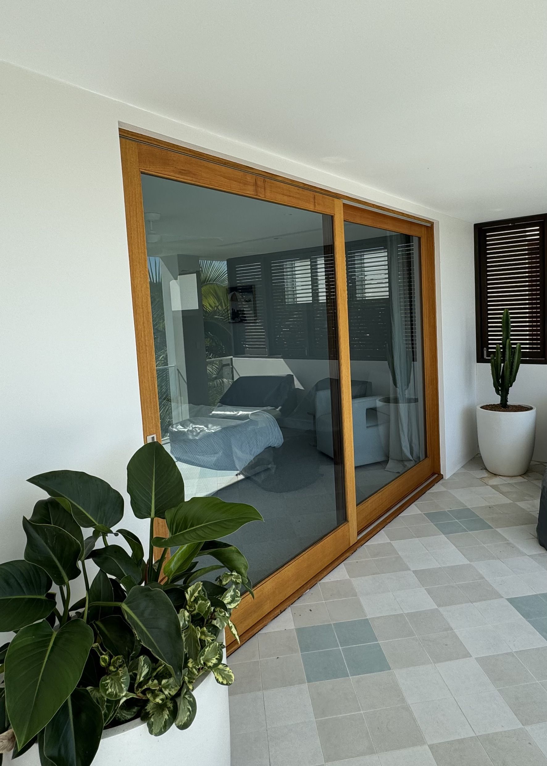 Bright Patio With Sliding Glass Doors, Potted Plants, and a Tiled Floor Beside a Bedroom Interior — Fineworx Joinery in Warnervale, NSW