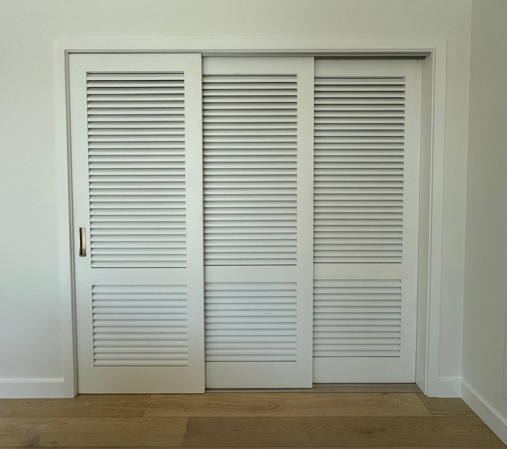 White Louvered Closet Doors in a Minimalist Room With Light Walls and Wood Flooring — Fineworx Joinery in Warnervale, NSW