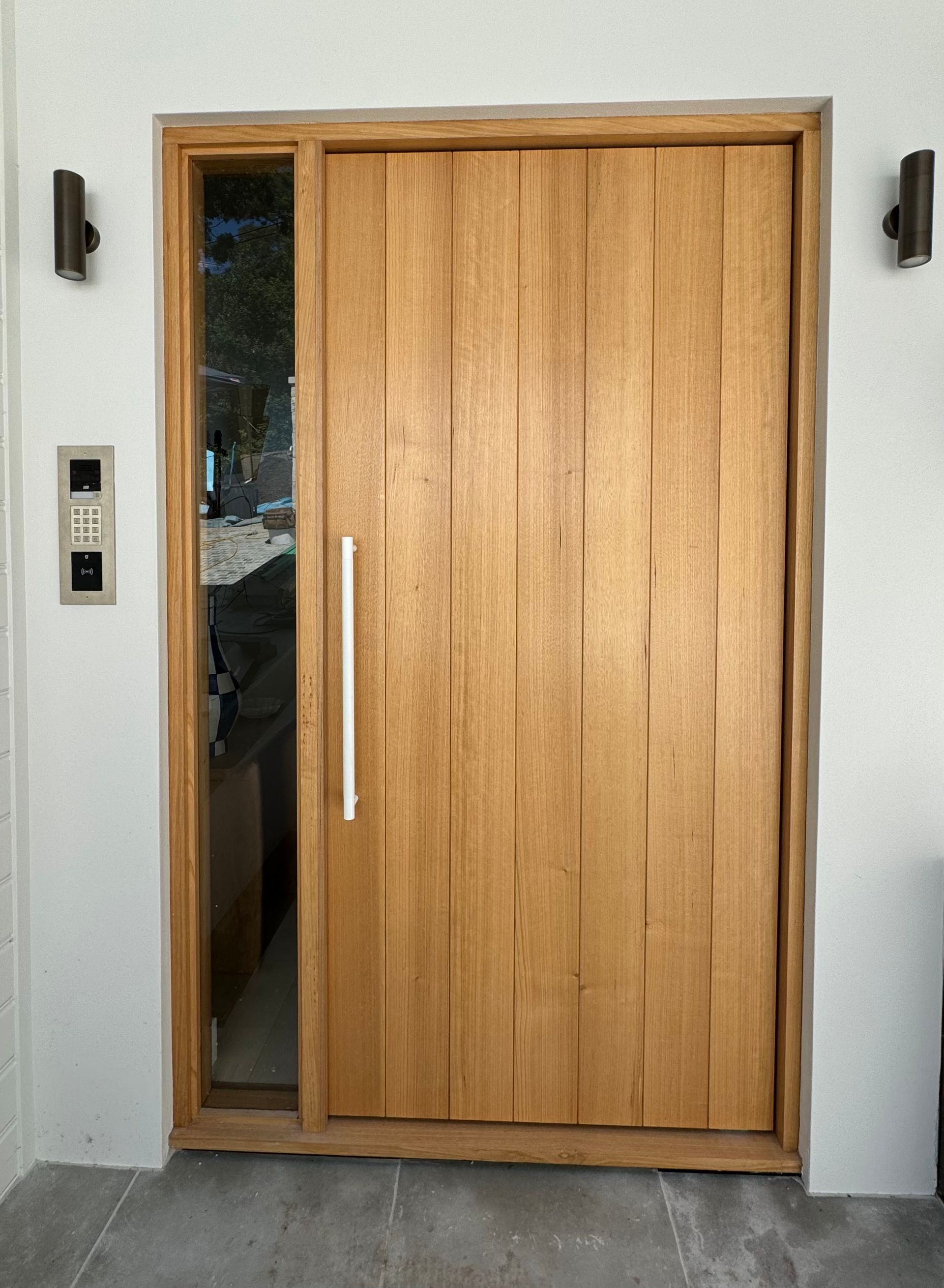 Wooden Front Door With Vertical Glass Panel, Set in a White Exterior Wall With Wall-mounted Lights — Fineworx Joinery in Warnervale, NSW