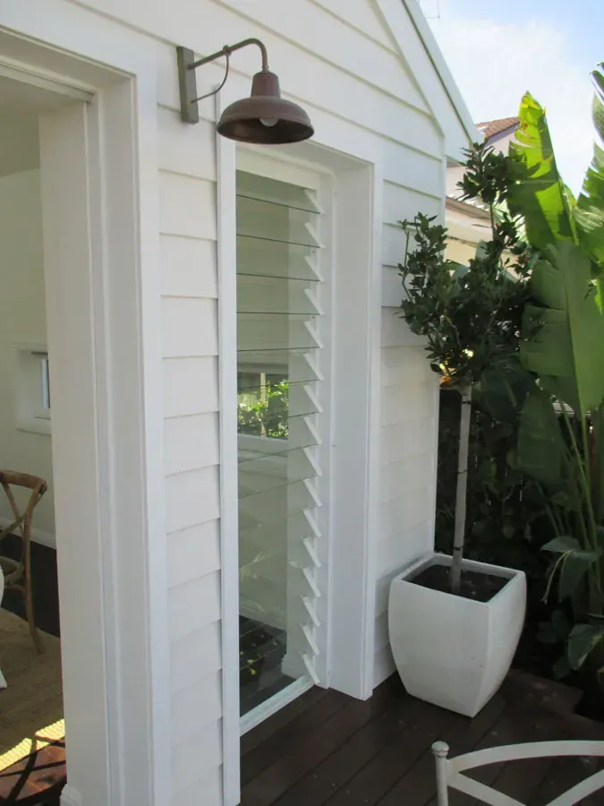 Narrow side patio with white shutters, dark wall lantern, and a potted plant beside a doorway — Fineworx Joinery in Warnervale, NSW
