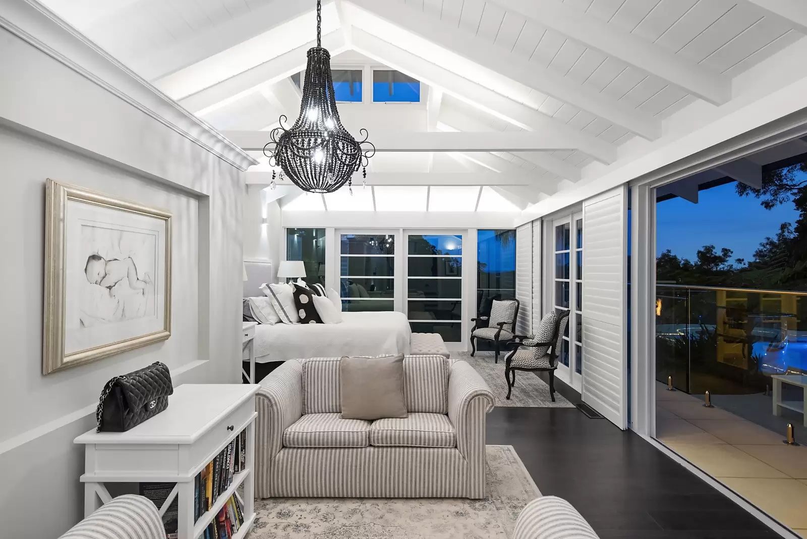 Bright white vaulted living room with sofa, chandelier, and large windows opening to a lit balcony at dusk — Fineworx Joinery in Warnervale, NSW