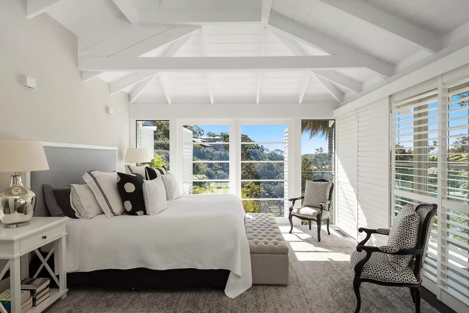 Bright white bedroom with vaulted ceiling, bed, chairs, and large windows overlooking the water — Fineworx Joinery in Warnervale, NSW