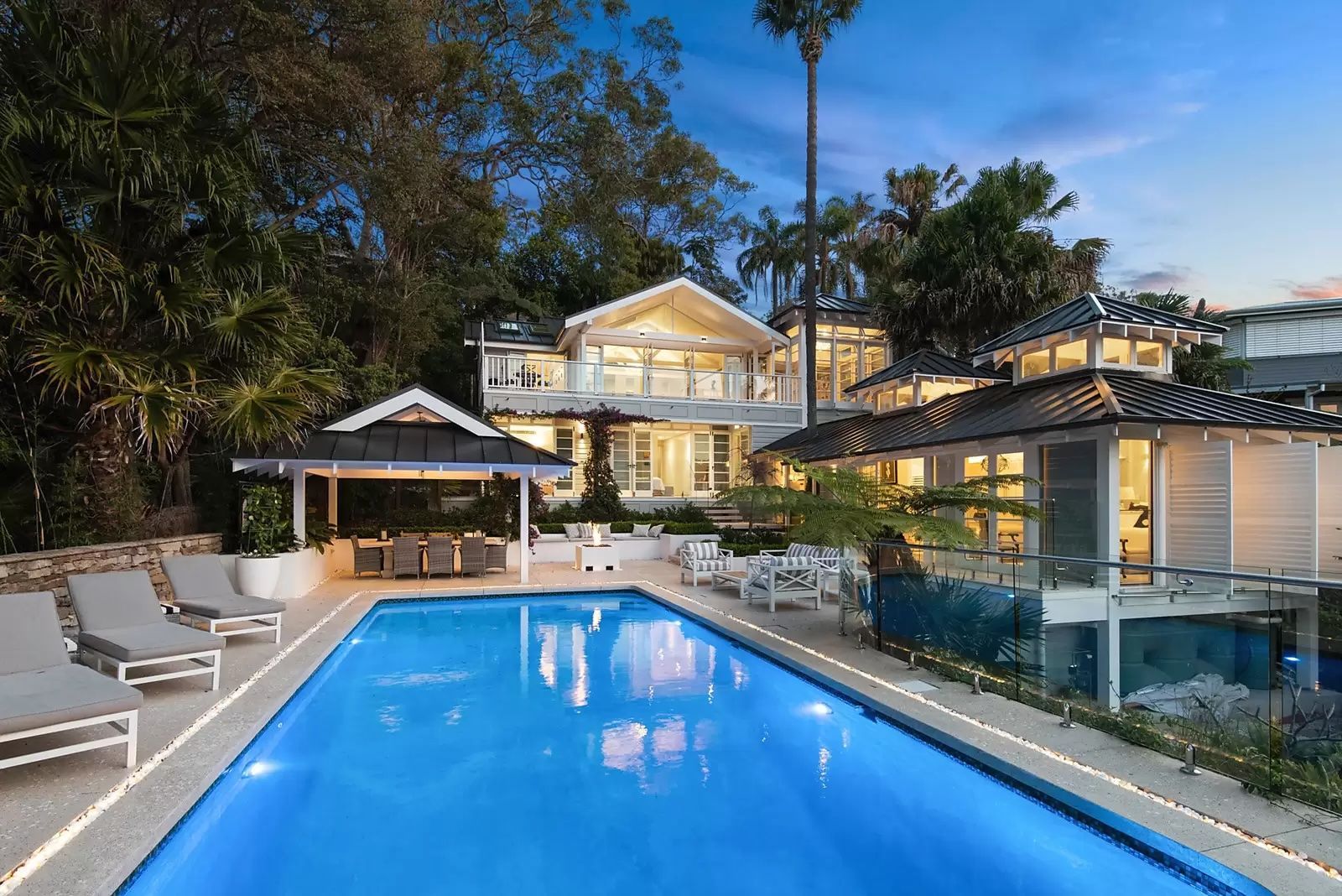 Luxury house with a glowing pool at dusk, surrounded by tropical trees and patio seating — Fineworx Joinery in Warnervale, NSW