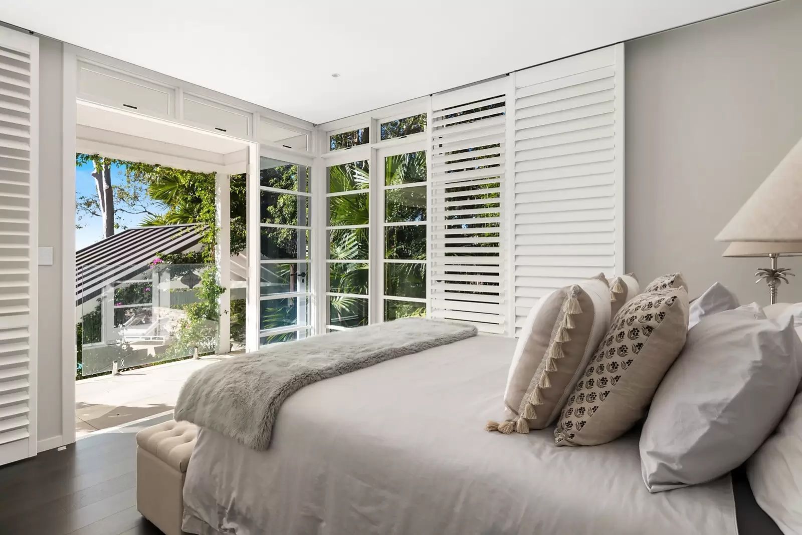 Bright bedroom with white shutters, large windows, and a bed with neutral pillows and a gray throw. — Fineworx Joinery in Warnervale, NSW