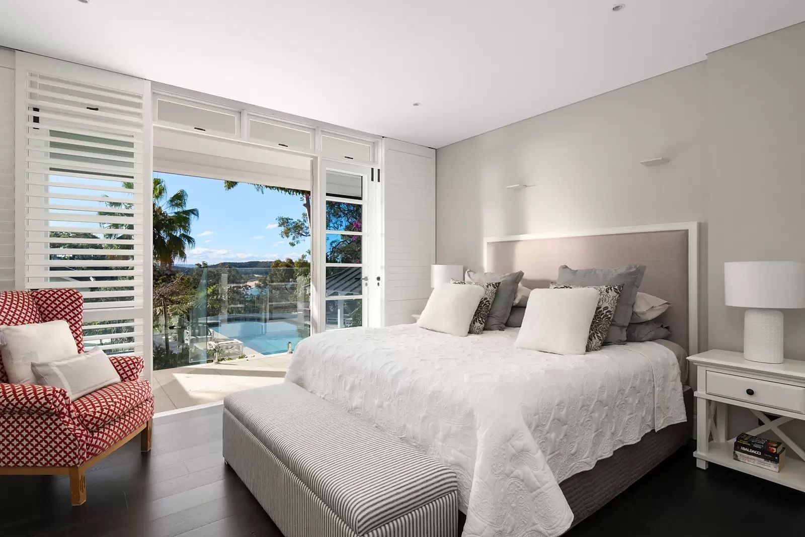 Bright bedroom with white bed, pink chair, and large window overlooking a pool and ocean — Fineworx Joinery in Warnervale, NSW