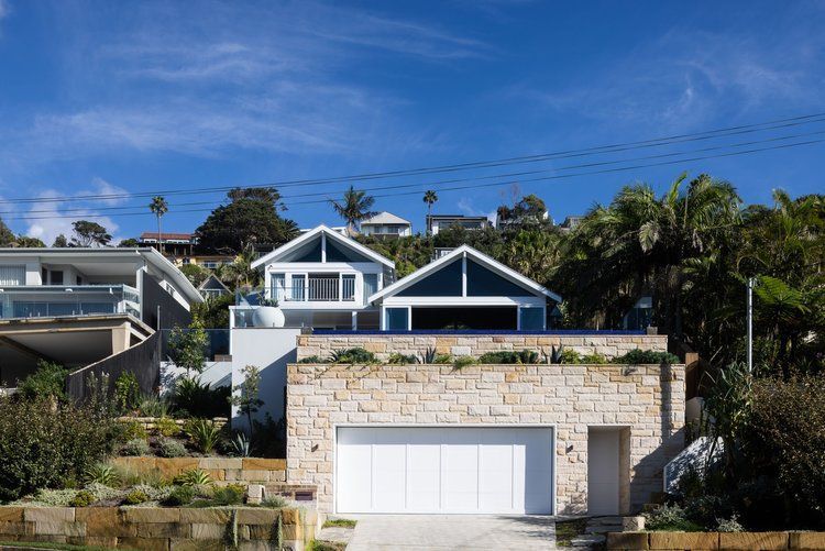 Modern house with stone garage and white trim on a sunny hillside street — Fineworx Joinery in Warnervale, NSW