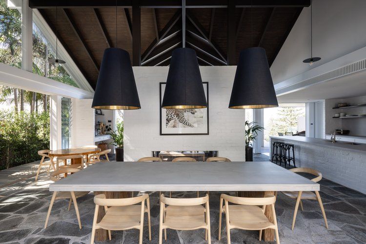 Modern open-plan dining room with a long table, black pendant lights, and kitchen beyond — Fineworx Joinery in Warnervale, NSW