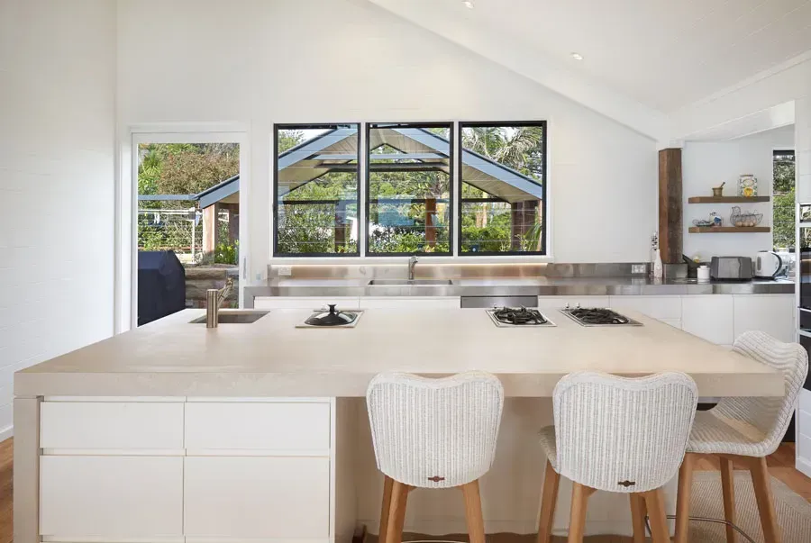 Bright white modern kitchen with island, woven stools, and large windows overlooking greenery — Fineworx Joinery in Warnervale, NSW
