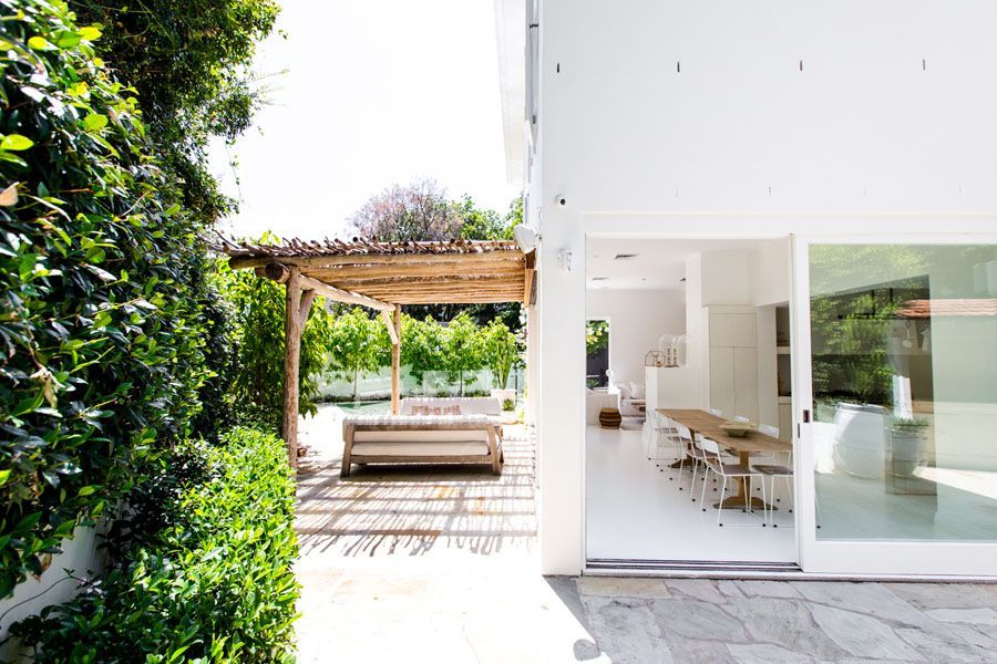 Modern white patio with pergola, outdoor seating, and large sliding glass doors by a lush green wall — Fineworx Joinery in Warnervale, NSW
