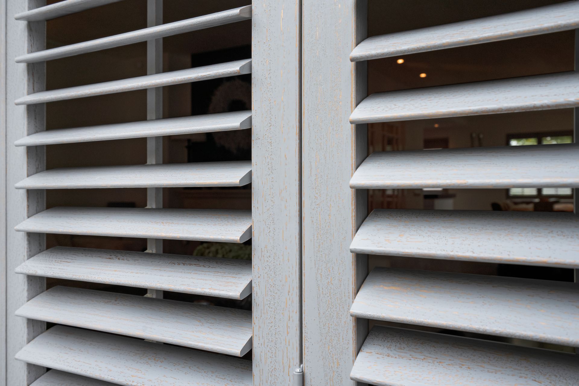 Close-up of white window blinds with a narrow gap showing a dim room inside — Fineworx Joinery in Warnervale, NSW