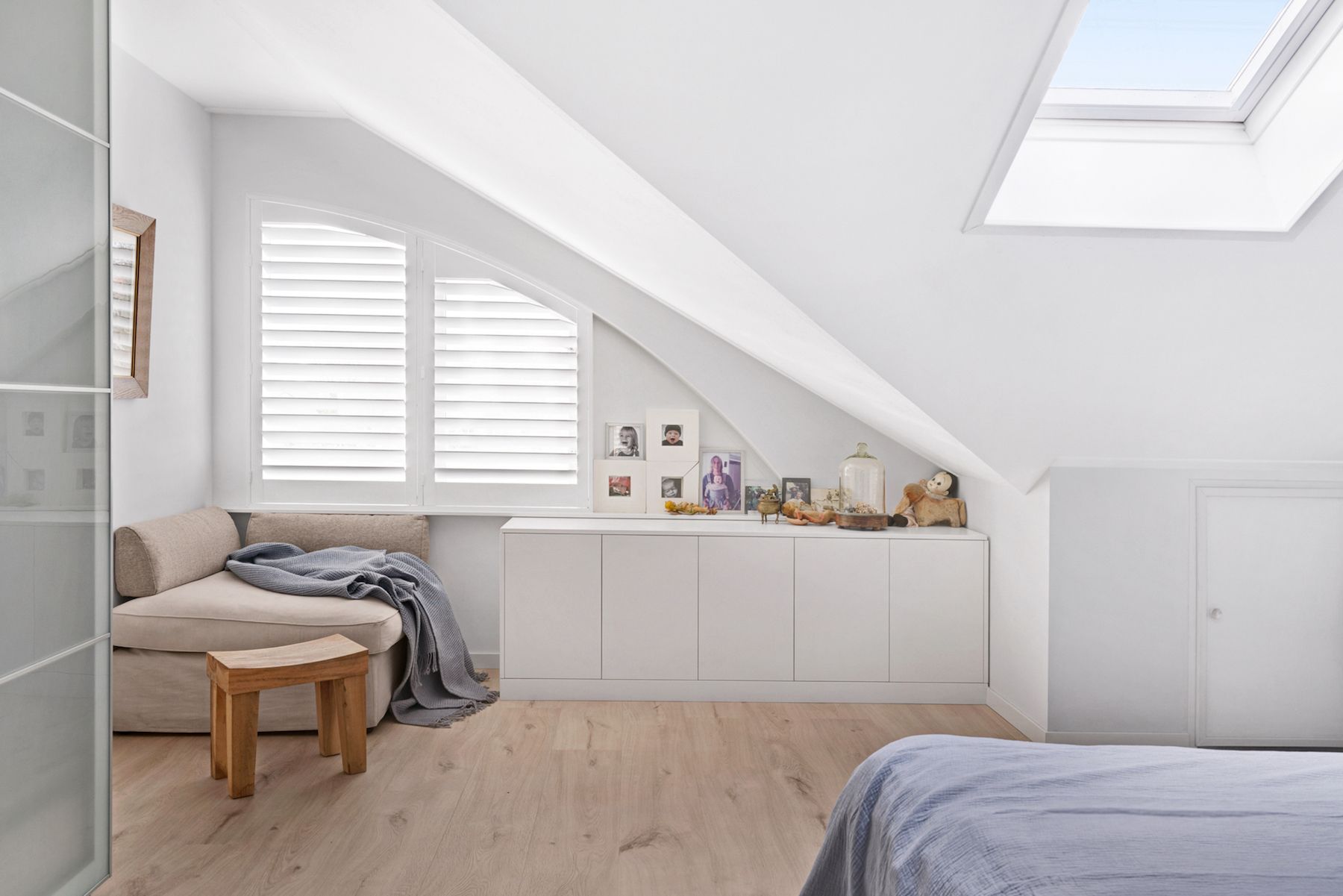 Bright white attic bedroom with skylight, low windows, bed, bench, and built-in storage cabinets. — Fineworx Joinery in Warnervale, NSW